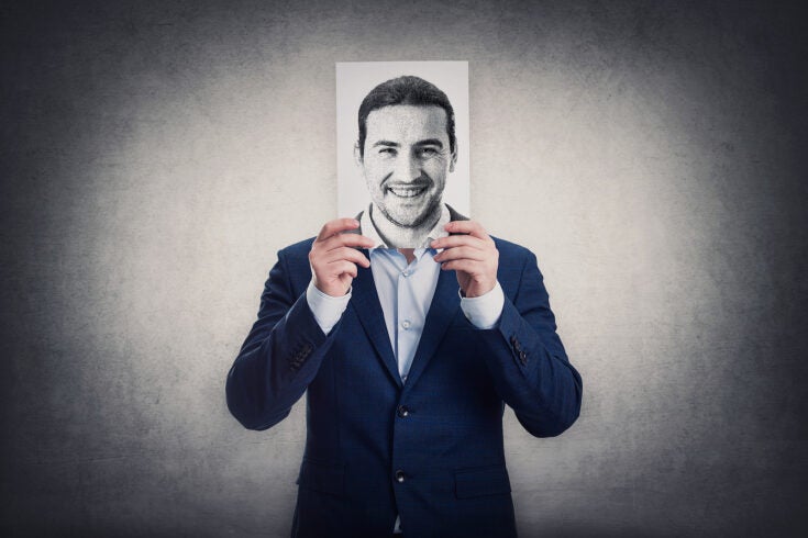 a business man hides his head behind a drawing of a smiling face