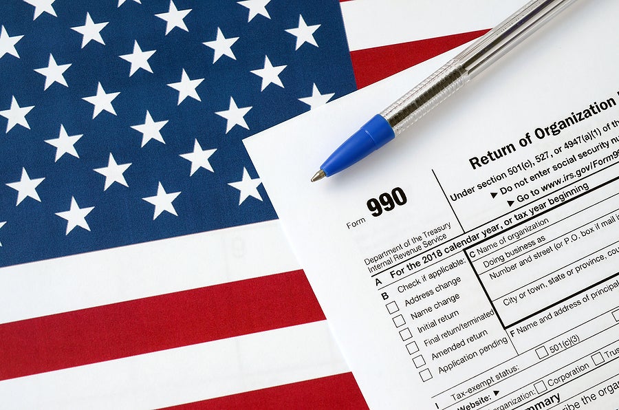 Form 990 Return of organization exempt from income tax and blue pen on United States flag. Internal revenue service tax form
