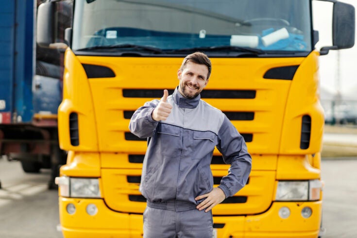 a commercial truck driver smiling and giving a thumbs up