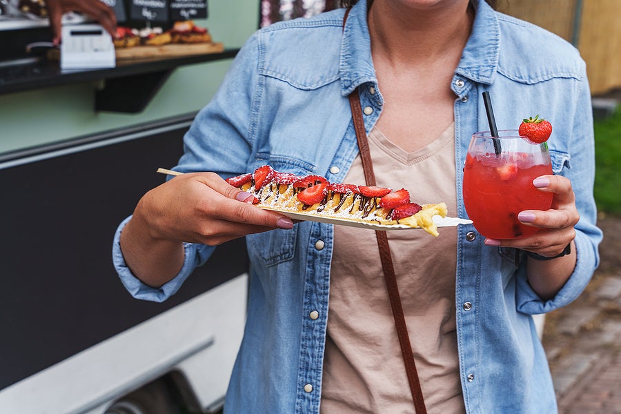 Woman enjoys delicious pancakes with strawberries and strawberry daiquiri at a food festival. Crepes with fresh strawberries and whipped cream, street food. Food trucks, food festival