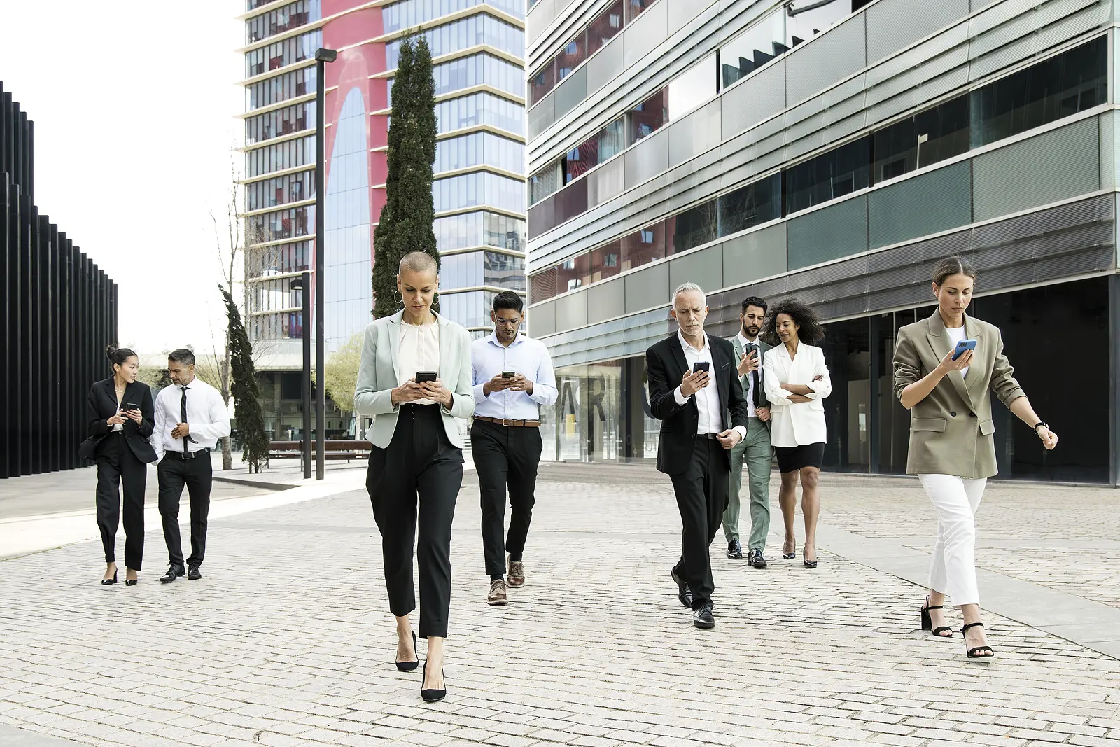 Group of confident business people walking the street using their phones. Diverse team of focused businesswoman and businessman walking outside while texting on their smartphones.