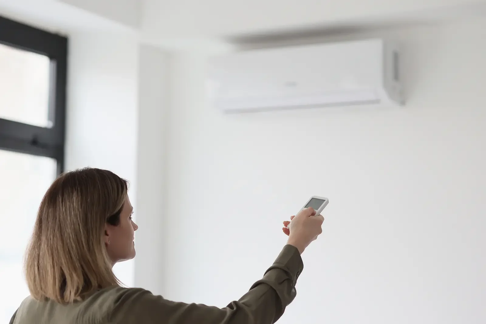 Woman uses remote control to adjust air conditioner in light office. Stabilization of temperature in premise for comfortable work closeup