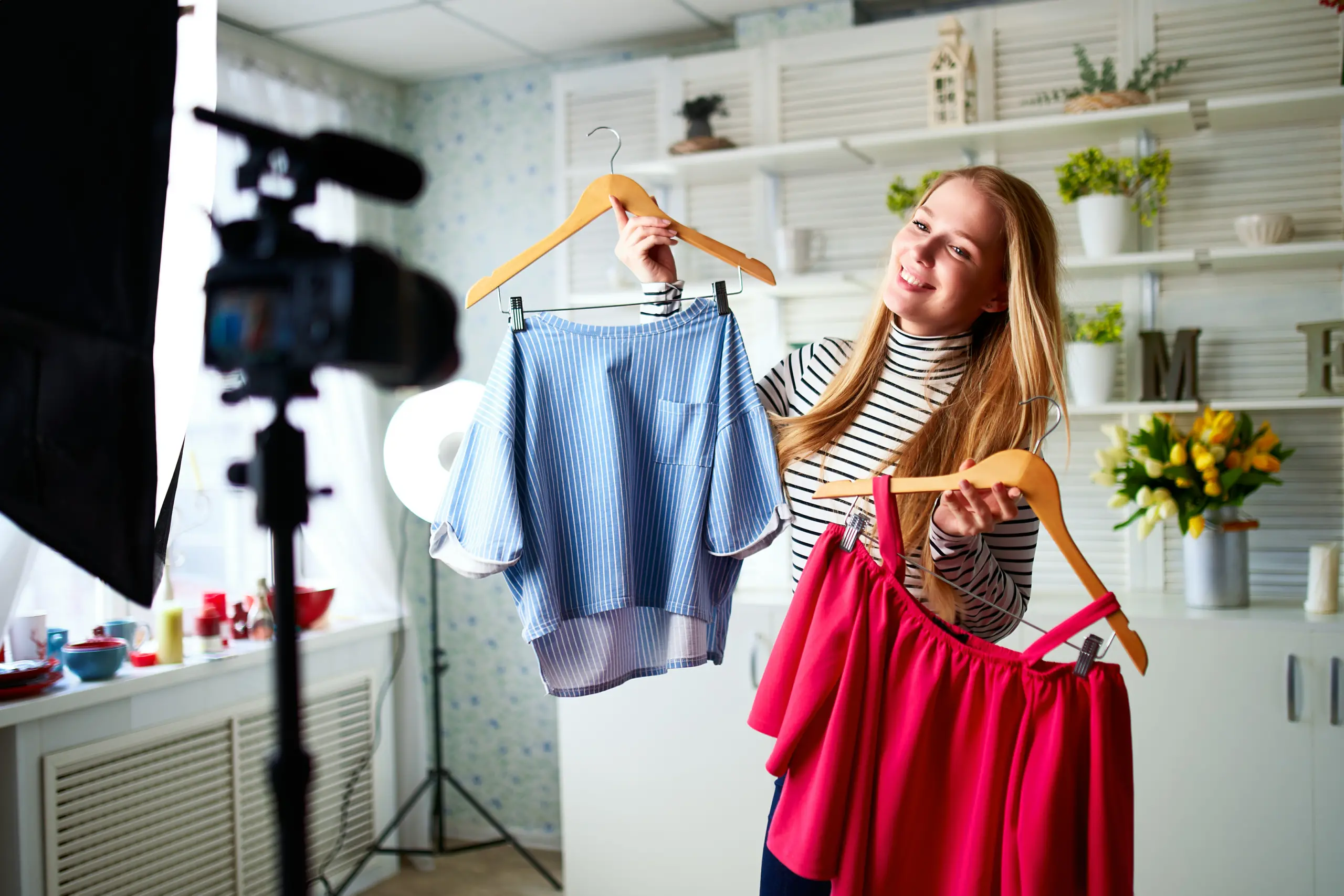Fashion blogger woman in jeans and turtleneck showing casual colorful shirts on camera. Stylist influencer female shows trendy clothes filming vlog episode for her channel. Opinion leader sets trends.