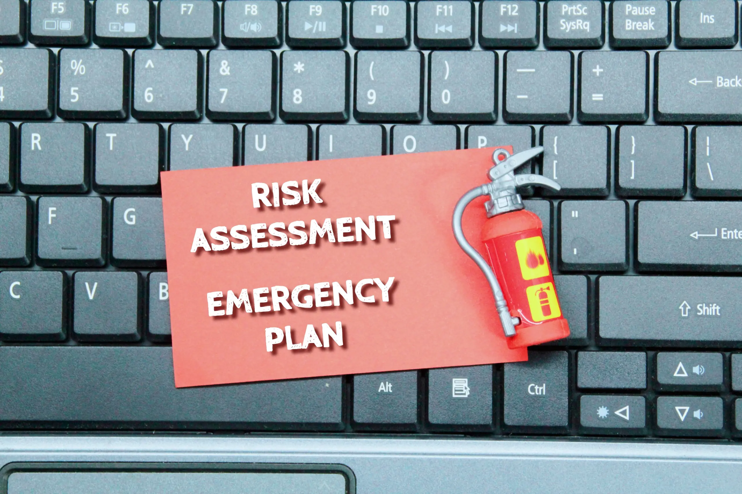 laptop keyboard, fire extinguisher, colored paper with the words risk assessment and emergency Plan