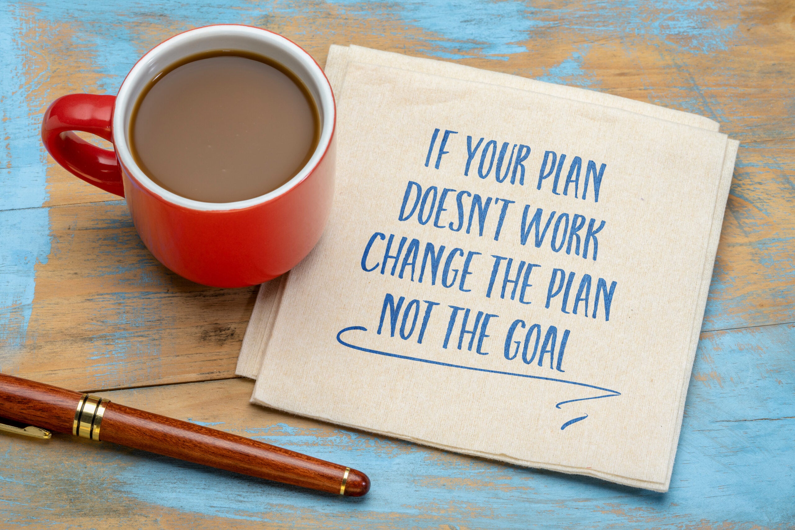 a coffee, a pen, and a napkin with the words "If your plan doesn't work, change the plan not the goal"