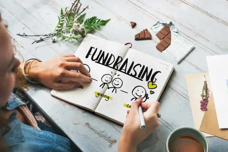 a person writing in a notebook the word "fundraising"