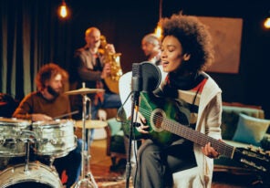 a woman playing guitar with a band behind her in a small studio