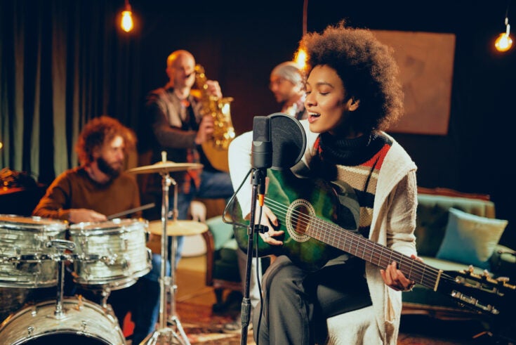 a woman playing guitar with a band behind her in a small studio