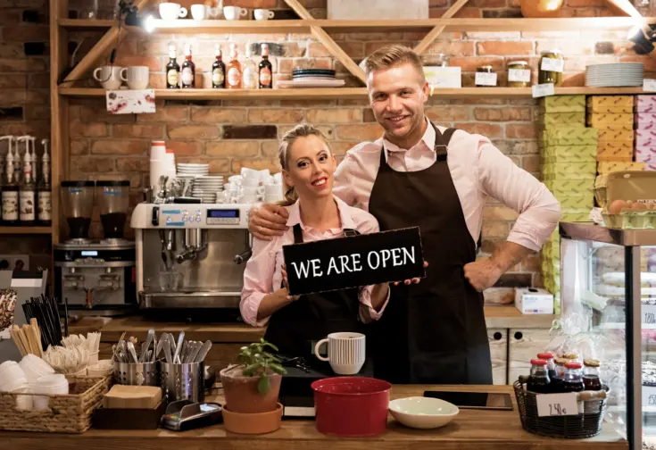 two business owners proudly displaying their "We Are Open" sign in their newly opened cafe