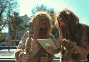 a comical depiction of two cavemen using a modern tablet device