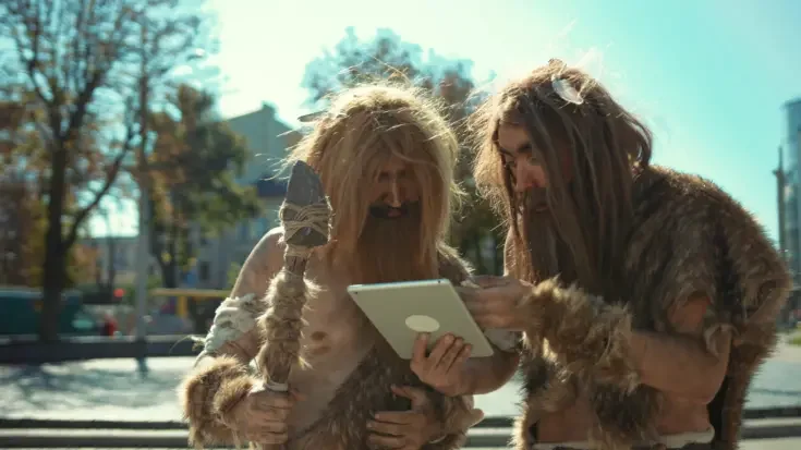 a comical depiction of two cavemen using a modern tablet device