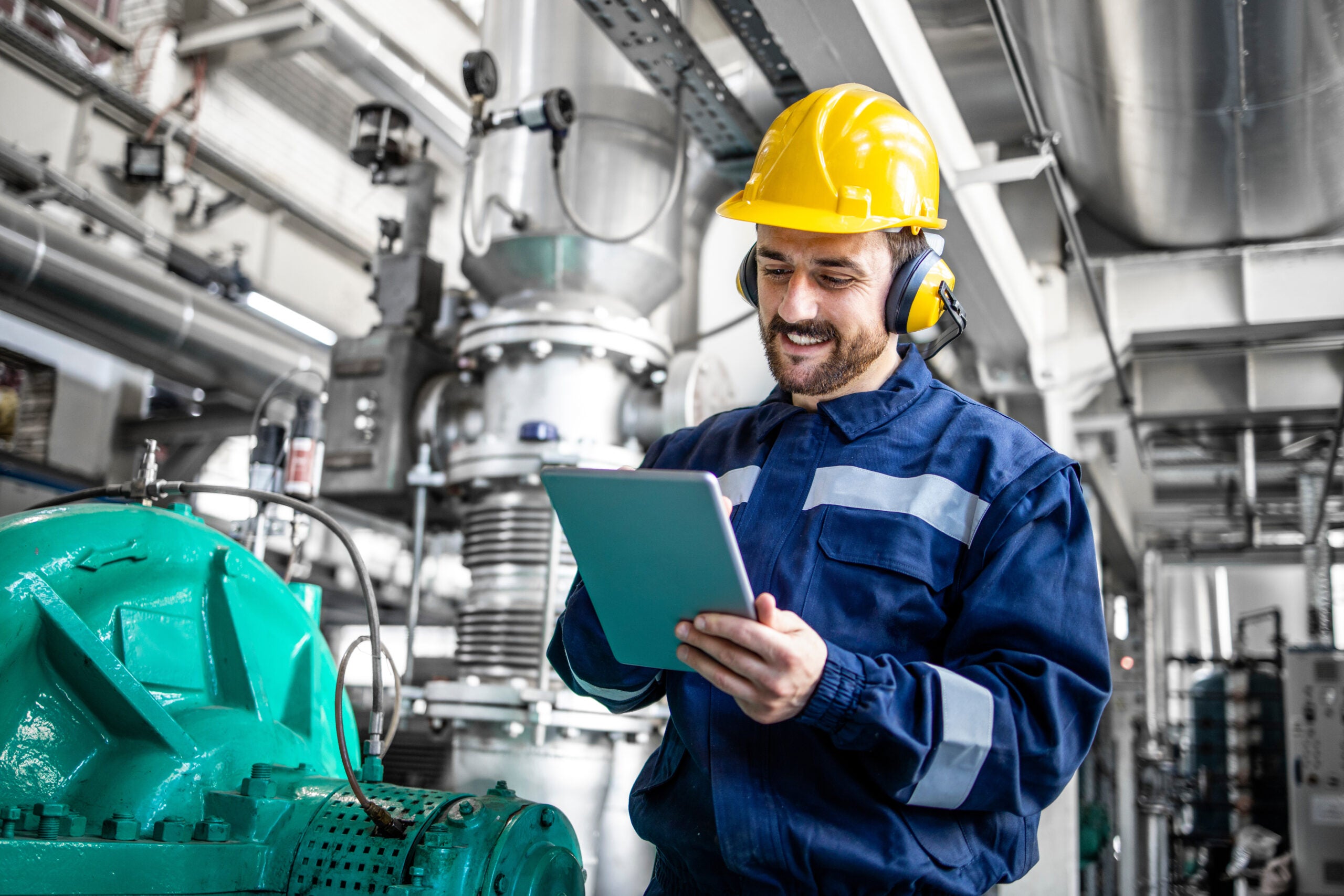 Industrial engineer standing by gas generator in power plant and controlling electricity production on his tablet.