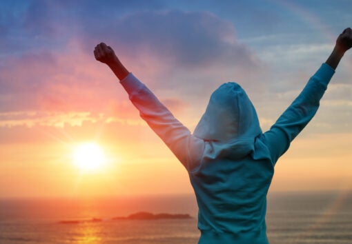 Sport and life achievements and success concept. Rear view sporty girl raising arms towards beautiful glowing sunshine.
