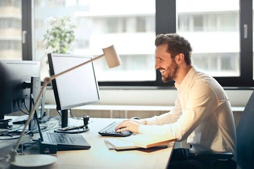 A man sitting at a desk smiling while working on the computer.