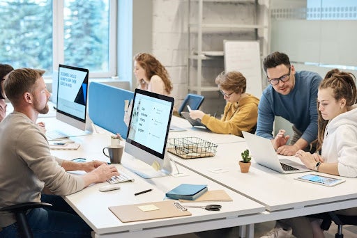 Six people working on their computers at a communal table.