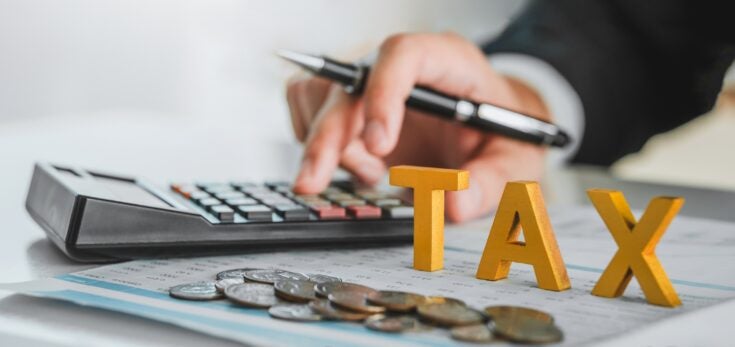 a close up view of a hand using a calculator with the word "TAX" in bold block-like letters