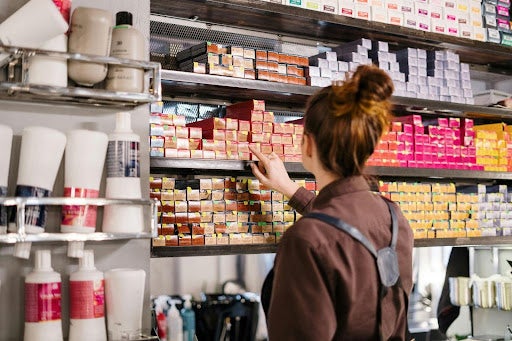 A salon owner selecting a product from a variety of colorful boxes on the shelves in their salon.