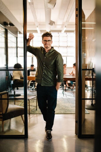 A man smiling and standing in an open doorway to an office