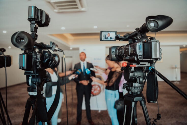 video cameras pointed at a man giving an interview to a group of reporters