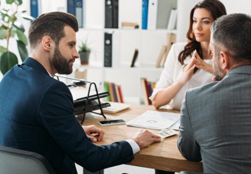 selective focus of handsome investors in suits talking with attractive advisor at workspace