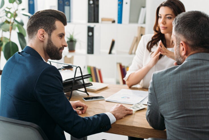 selective focus of handsome investors in suits talking with attractive advisor at workspace
