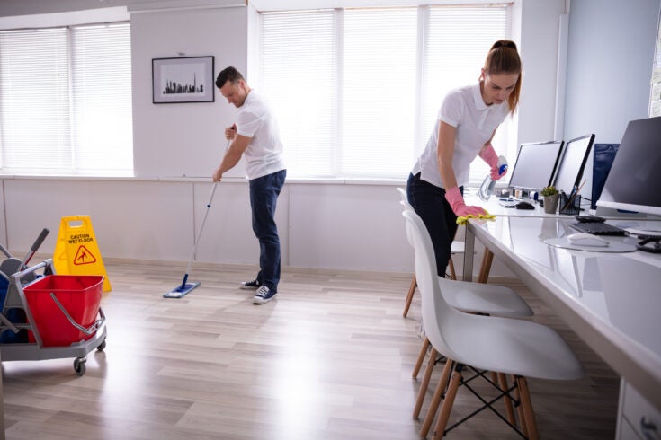 Two Smiling Young Janitor Cleaning The Desk And Mopping Floor In The Office