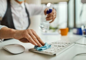 Close-up of businesswoman disinfecting computer keyboard in the office.