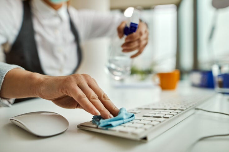 Close-up of businesswoman disinfecting computer keyboard in the office.
