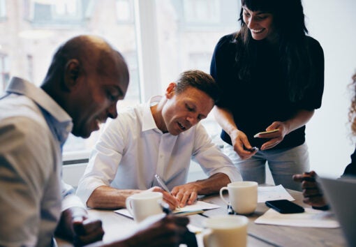 Manager signing paperwork while working with a diverse team of colleagues around a boardroom table in an office