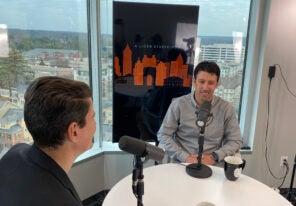 Man in gray shirt speaking with podcast host at table