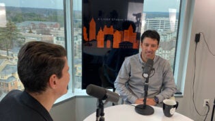 Man in gray shirt speaking with podcast host at table