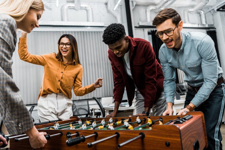 multicultural business colleagues playing table football together in office