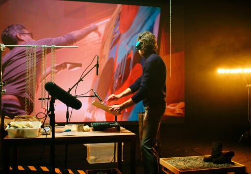 Anonymous man imitating and recording sounds of brush strokes on canvas against screen with footage of artist creating painting in workshop