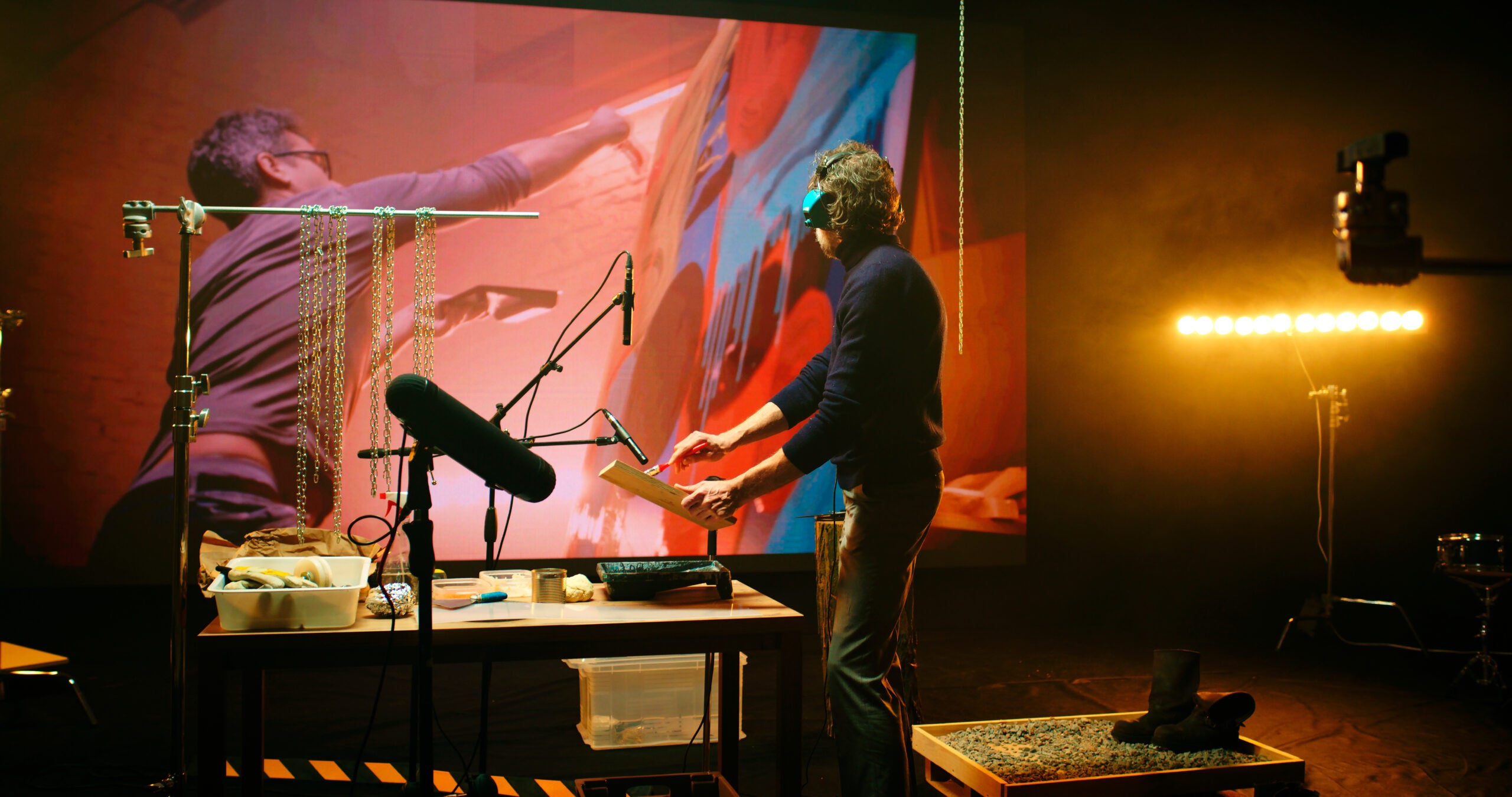 Anonymous man imitating and recording sounds of brush strokes on canvas against screen with footage of artist creating painting in workshop