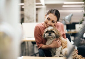 Young happy businesswoman holding her dog while taking a break from work in the office.