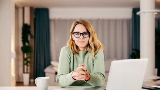 A middle-aged woman working online from her comfortable home and looking at the camera.