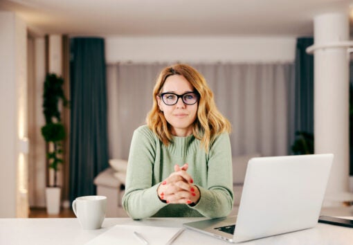A middle-aged woman working online from her comfortable home and looking at the camera.