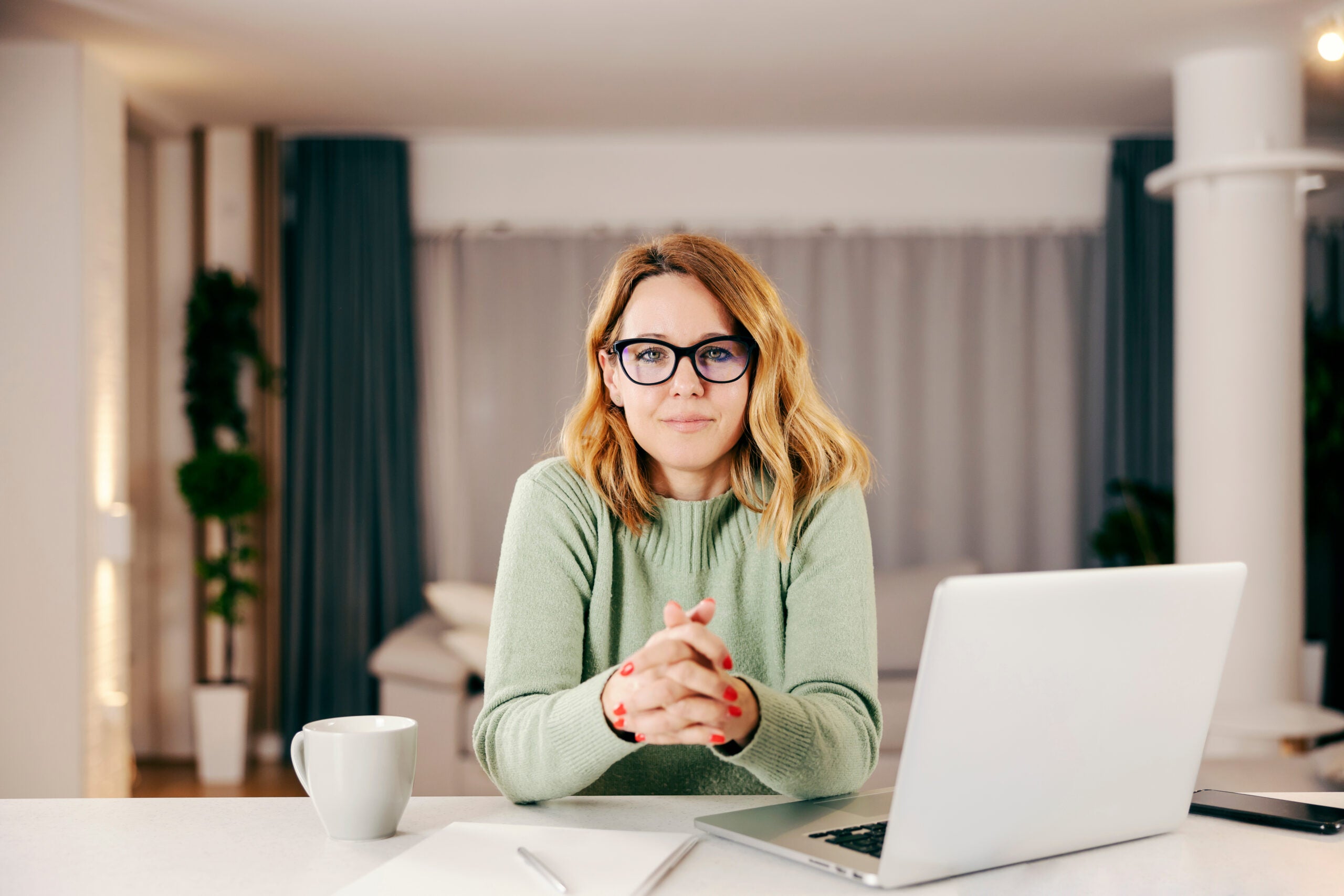 A middle-aged woman working online from her comfortable home and looking at the camera.