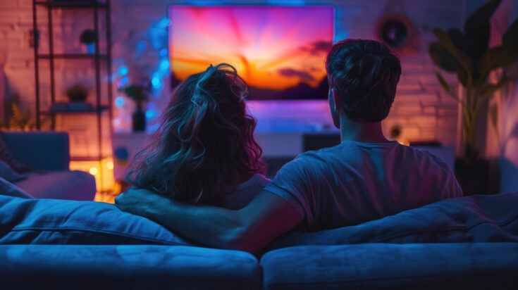 Couple watch tv together at home. Modern television. Cozy living room interior background. Cute happy people enjoy interesting movie back view. Online cinema concept. Fun evening leisure.