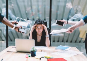 Young disappointed woman feeling headache from deadline surrounded by colleagues at workplace, multi-purpose female employee,tired of work and exhausted, stress in office. Overworked female in confuse