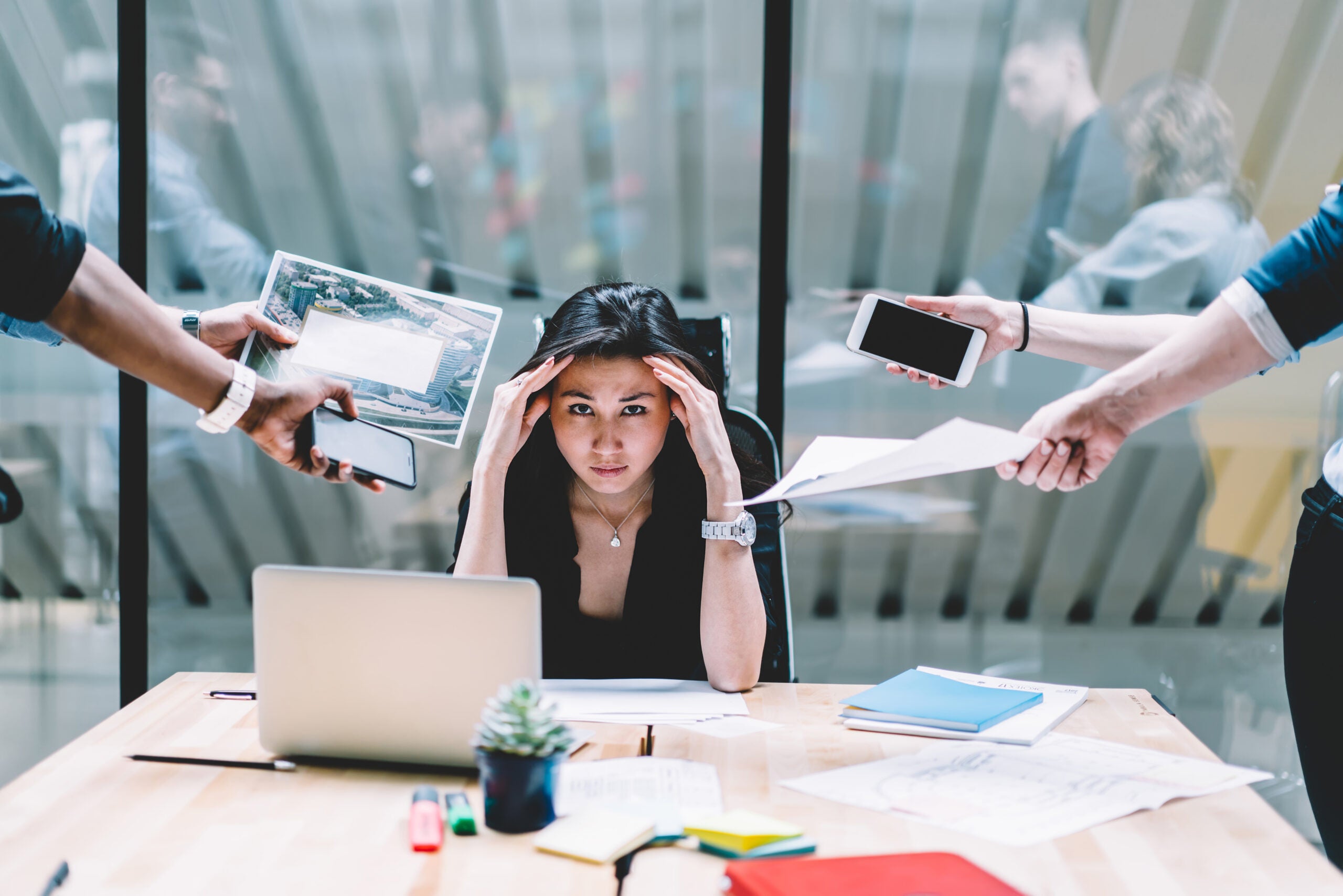 Young disappointed woman feeling headache from deadline surrounded by colleagues at workplace, multi-purpose female employee,tired of work and exhausted, stress in office. Overworked female in confuse