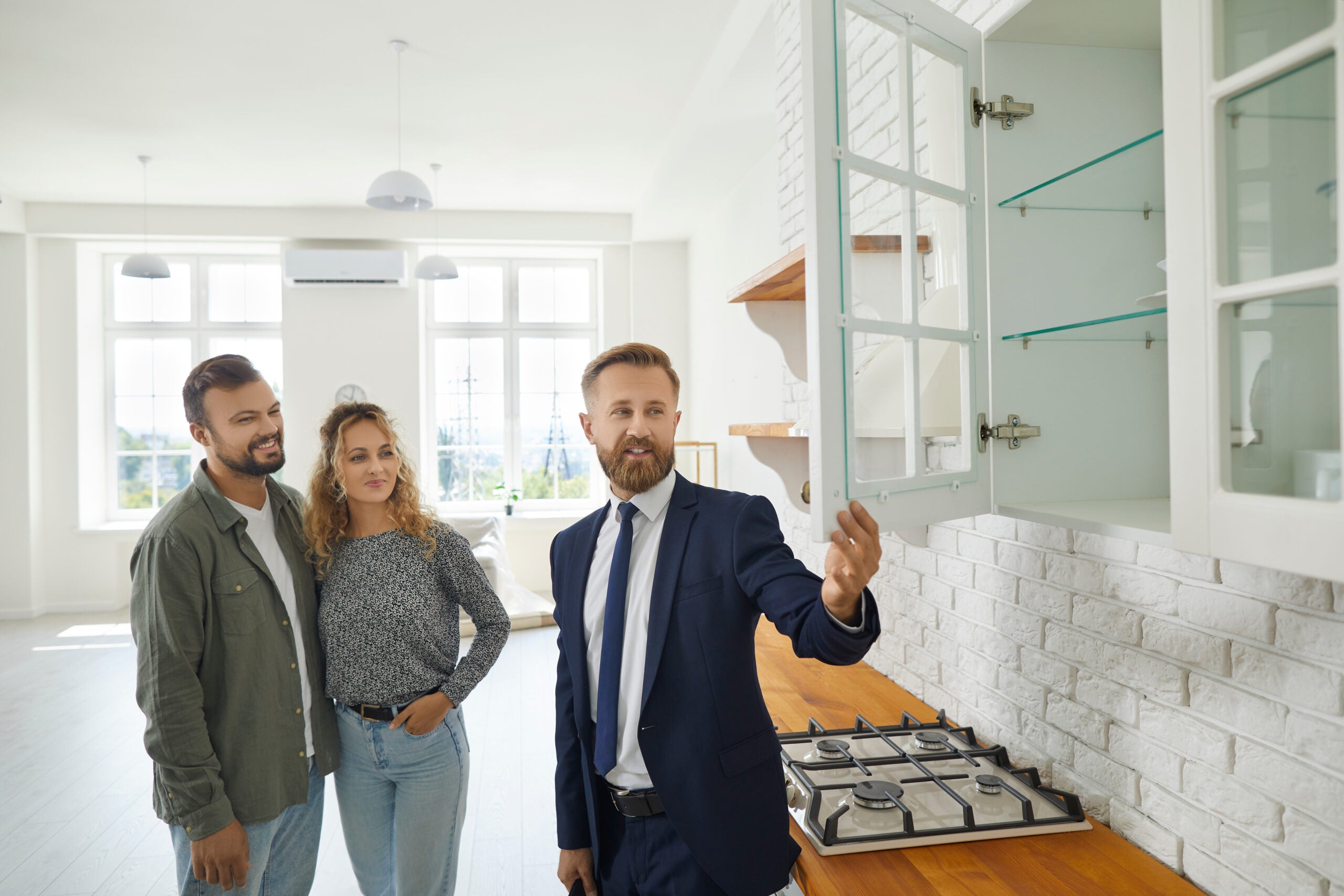 Real estate agent giving first time buyers or future tenants tour about new home. Boyfriend and girlfriend buying modern house.Husband and wife consulting expert on good quality wooden kitchen cabinet