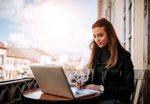 Young bussines woman working outdoors. Writting in a notebook while sitting in front of a laptop.