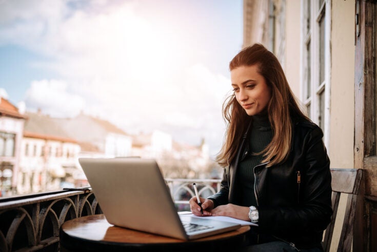 Young bussines woman working outdoors. Writting in a notebook while sitting in front of a laptop.