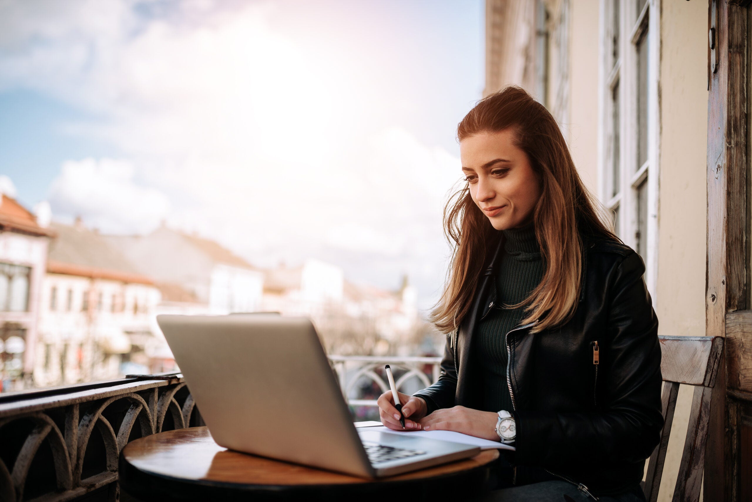 Young bussines woman working outdoors. Writting in a notebook while sitting in front of a laptop.