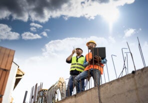 Men in hardhat and yellow and orange jacket posing on building s