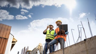 Men in hardhat and yellow and orange jacket posing on building s