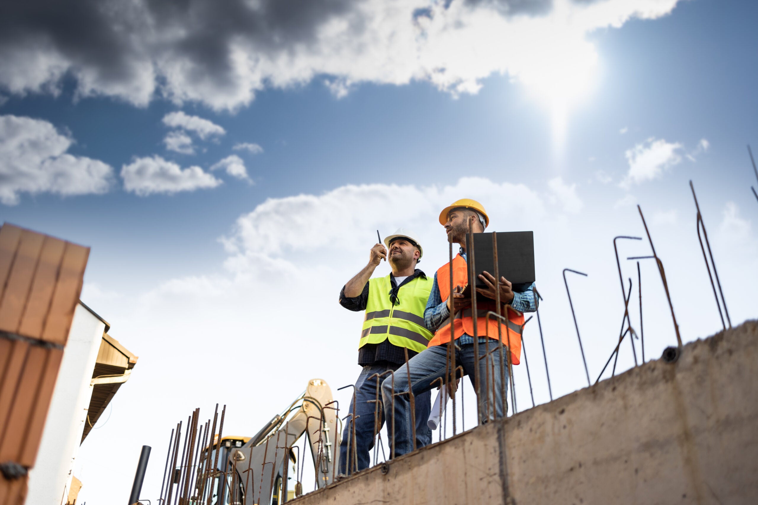 Men in hardhat and yellow and orange jacket posing on building s