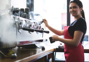 Smiling young trainee in uniform learning how to temperate drinks with steam