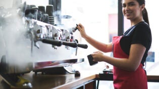 Smiling young trainee in uniform learning how to temperate drinks with steam